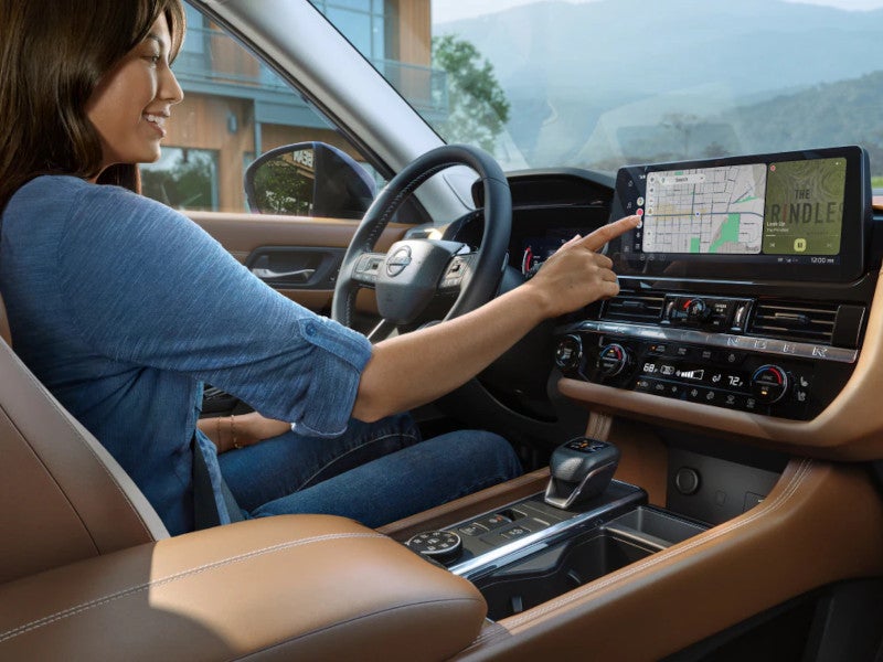 Driver using the touchscreen navigation display in the 2026 Nissan Pathfinder, with a brown leather interior