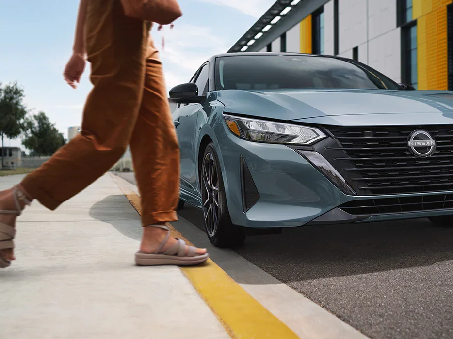 person-walking-past-front-view-parked-nissan-sedan